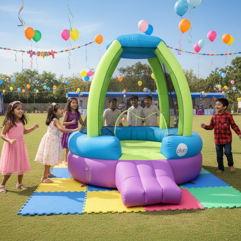 Children playing around a colorful inflatable slide in a birthday party on a grassy field with balloons and flags in the background.